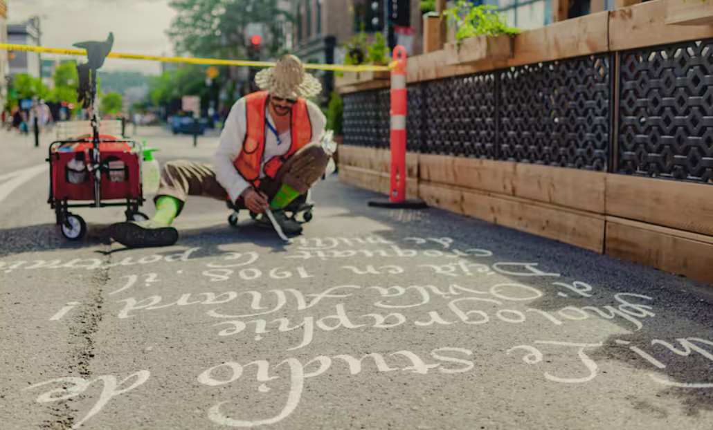 Romain Boz calligraphiant un texte à genoux sur l'asphalte de l'avenue Mont-Royal