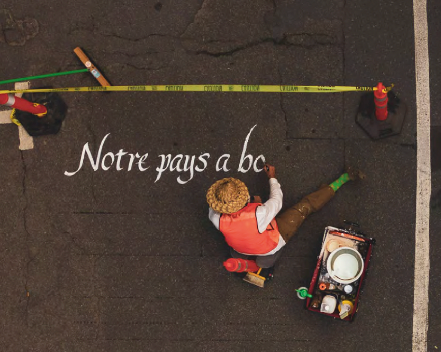 Artiste peignant les mots Notre pays a bc sur l'asphalte, vue aérienne avec ruban de chantier jaune