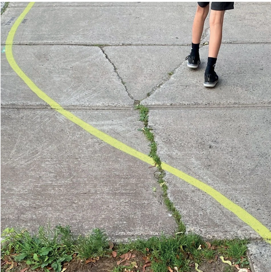Pieds sur le tracé jaune courbe au sol, herbe dans les fissures du béton
