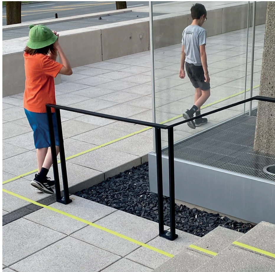 Enfant en orange regardant son reflet dans la façade vitrée du MNBAQ