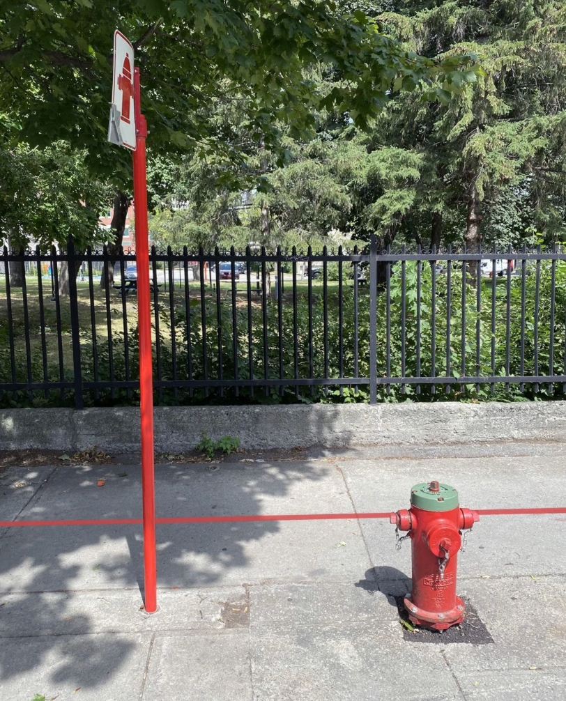 Borne-fontaine rouge et poteau de signalisation avec la ligne rouge du sentier traversant le trottoir