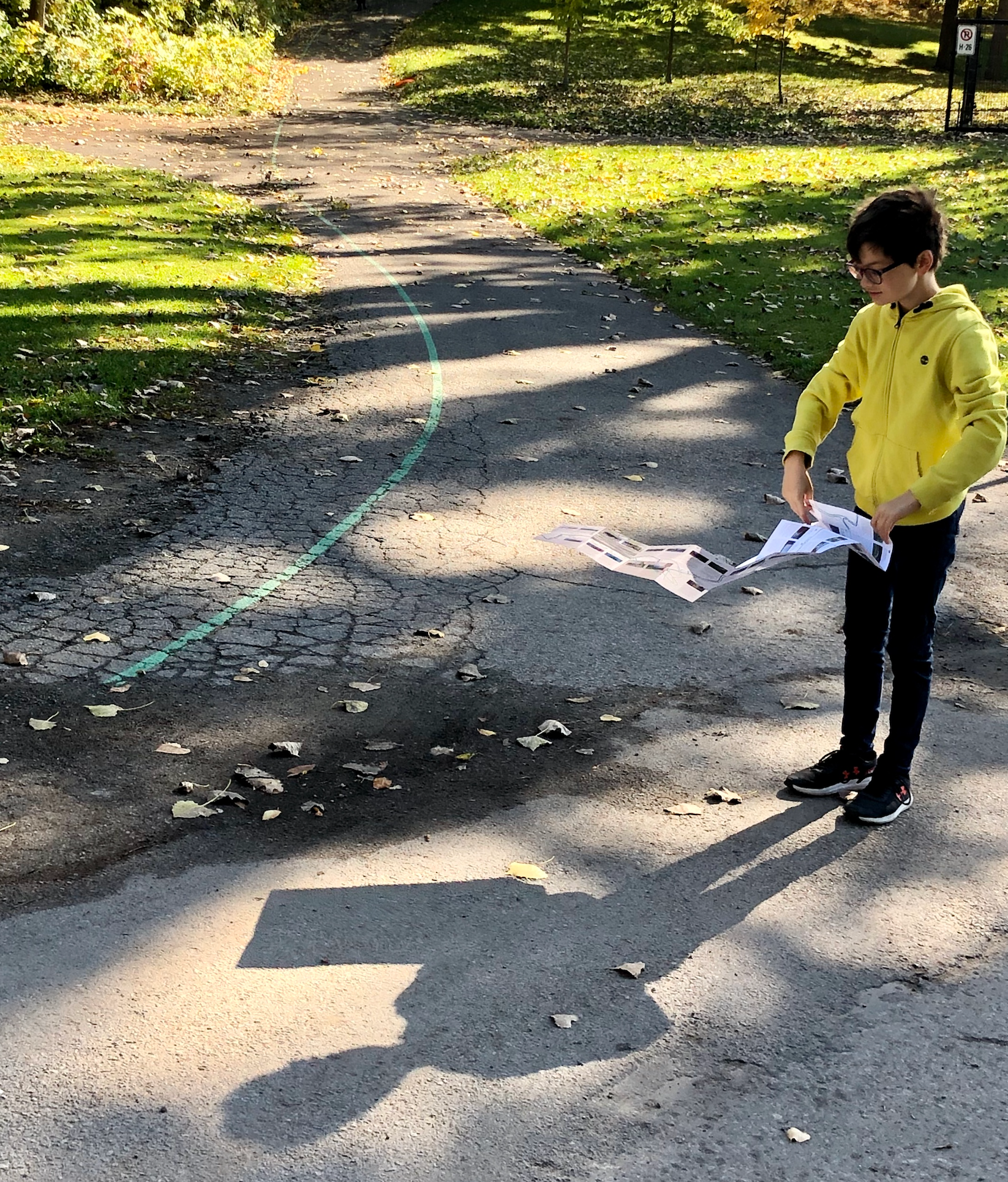 Enfant en veste jaune tenant des plans sur un sentier avec une ligne verte peinte au sol et une flèche