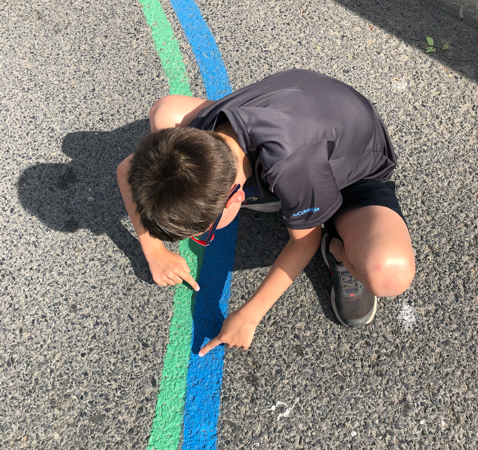 Enfant accroupi examinant de près les lignes verte et bleue peintes sur l'asphalte
