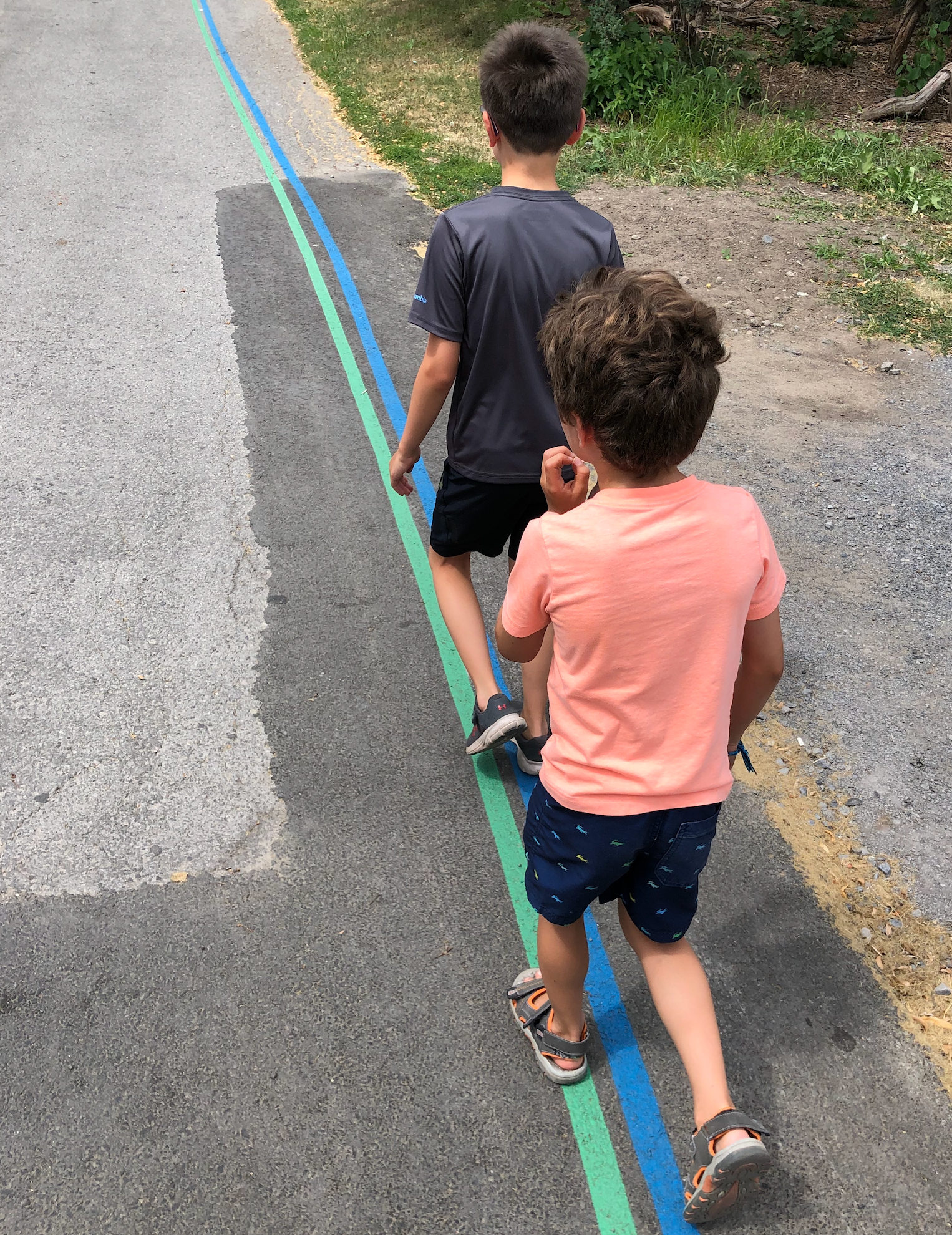 Deux enfants marchant côte à côte sur le sentier avec les lignes verte et bleue peintes sur la chaussée